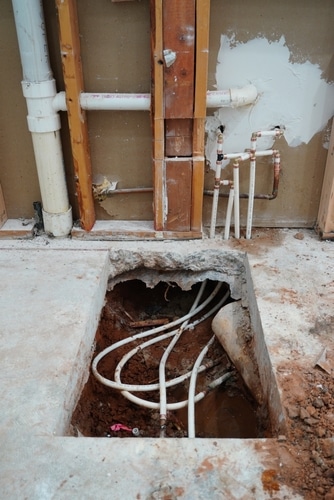 A square cut out of a concrete slab with pipes underneath