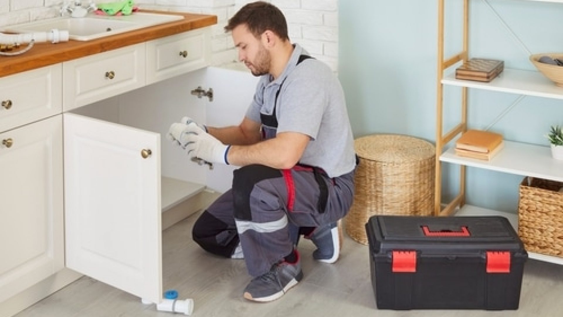 A plumber works on pipes under a kitchen sink.